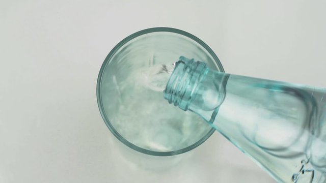 Water from a bottle pours into a glass cup in slow motion on a white background