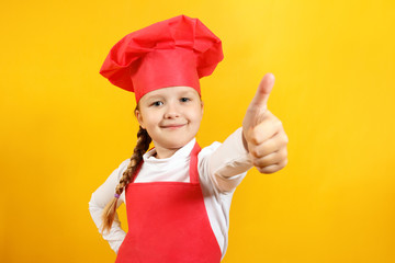 Beautiful girl dressed as a chef on a yellow background. The child shows a thumb up