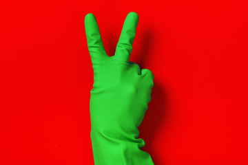 Victory sign in a protective glove of green color on a red background. Success concept