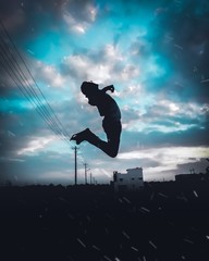 silhouette of a man jumping on background of blue sky