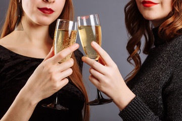 Beautiful glasses of champagne in women's hands. Ladies Look and smile into the camera, isolated on gray background