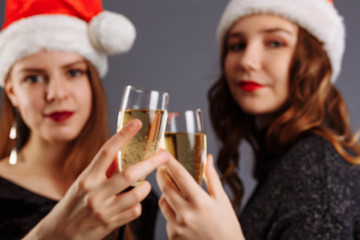 Two attractive cheerful girls with curly long hair in Christmas hat smiling, holding a champagne, posing to the camera, isolated on gray background