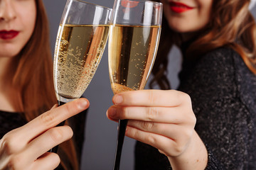 Beautiful glasses of champagne in women's hands. Ladies Look and smile into the camera, isolated on gray background