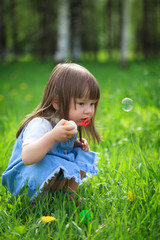 Little girl blows soap bubbles in the park in summer