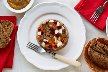 Aspic meat with vegetables and cranberries on a white plate 