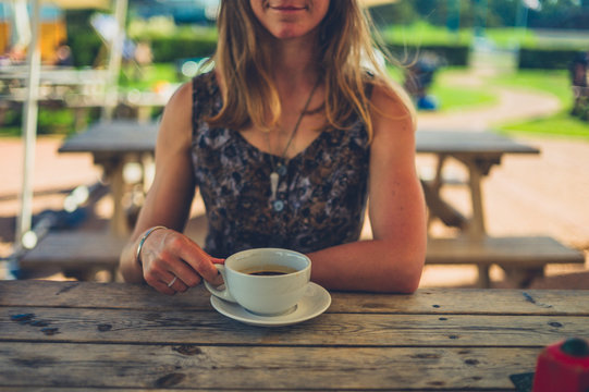 Young woman drinking coffee outdoors at cafe table