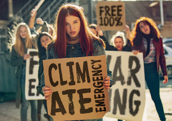 Young woman with poster in front of people protesting about climate changing on the street. Meeting about problem in ecology, environment, global warming, industrial influence, climate emergency.