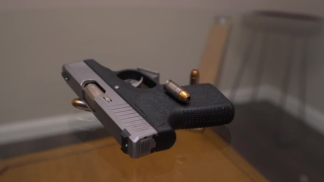 Rotating slider shot of small handgun and hollow point bullets sitting on glass table