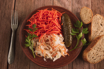 plate with pickled carrots, cabbage and cucumber on a wooden background