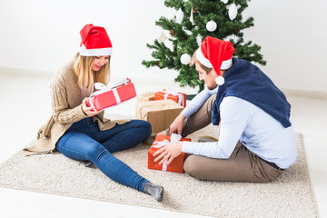 Fototapeta na wymiar Christmas and holidays concept - Young happy couple wearing santa hats opening gifts at home.