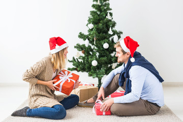 Christmas and holidays concept - Young happy couple wearing santa hats opening gifts at home.