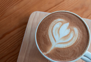 Latte coffee cup with latte art on wooden table in coffee shop.