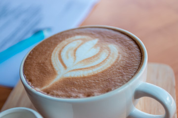 Latte coffee cup with latte art on wooden table in coffee shop.