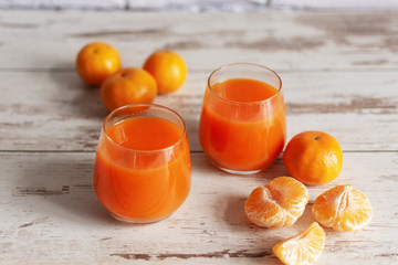 Glass of fresh tangerine juice with ripe tangerines on wooden table background.