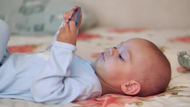 Little baby boy lies on the divan and holds in hands blue smartphone