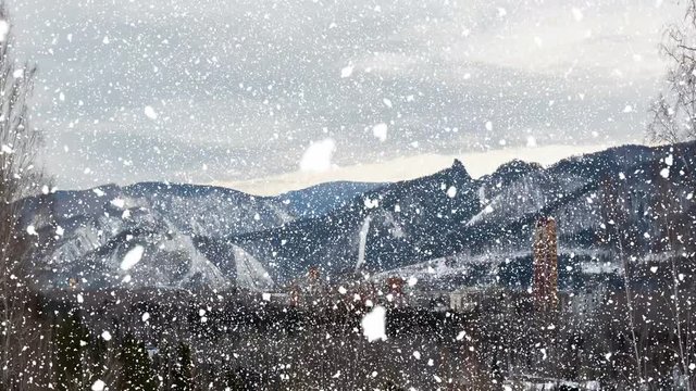 winter cityscape on the background of mountains, falling snow