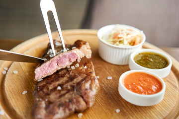 The waiter is holding a plate Grilled striploin steak with Pickled cabbage and two sauces. The strip steak, also called a New York strip. Serving on a wooden Board. Barbecue restaurant menu.