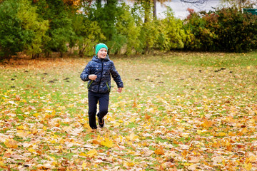 A boy runs across the lawn with autumn leaves