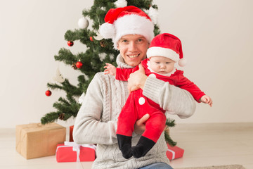 Father with his baby boy wearing Santa hats celebrating Christmas.