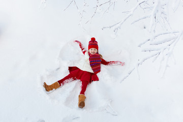 Child making snow angel. Kids winter outdoor fun.