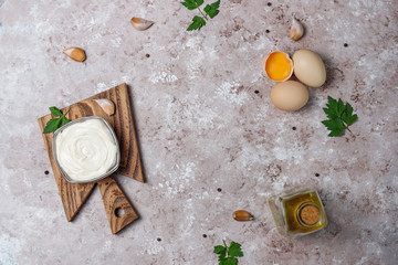 Mayonnaise sauce and ingredients on brown concrete background. Top view