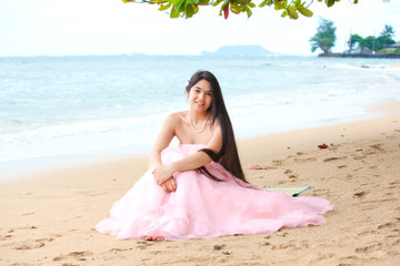 Fototapeta na wymiar Beautiful young woman in pink gown sitting on Hawaiian beach