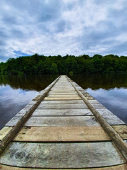 Long wooden walking pier on a lake in Fougeres, Brittany, France. Calm and still waters in the countryside.