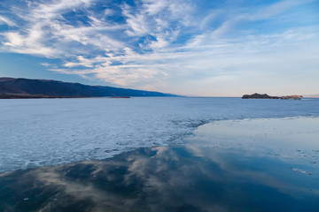 Baikal lake in may with cracking ice, water and reflection of blue sky with clouds