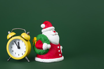 Cute gypsum colorful santa claus and yellow clock isolated over green background. New Year and Christmas concept.