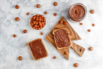 Chocolate spread or nougat cream with hazelnuts in glass jar on concrete background, copy space