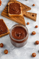 Chocolate spread or nougat cream with hazelnuts in glass jar on concrete background, copy space