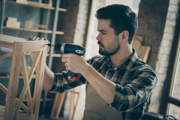 Profile photo of handsome guy building book shelf handmade design assembling using drill wooden industry home woodwork workshop indoors