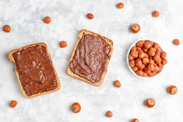 Chocolate spread or nougat cream with hazelnuts in glass jar on concrete background, copy space