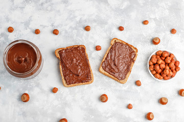 Chocolate spread or nougat cream with hazelnuts in glass jar on concrete background, copy space