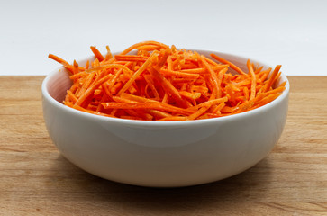 Carrots sliced in a white bowl, on wooden table