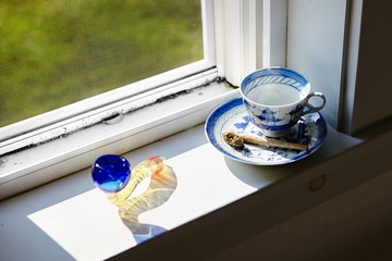 High angle shot of a marijuana blunt and dry cannabis on a coffee cup near the window