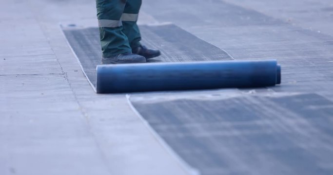 A worker unwinds a roll of ruberoid on a surface that needs to be isolated from water