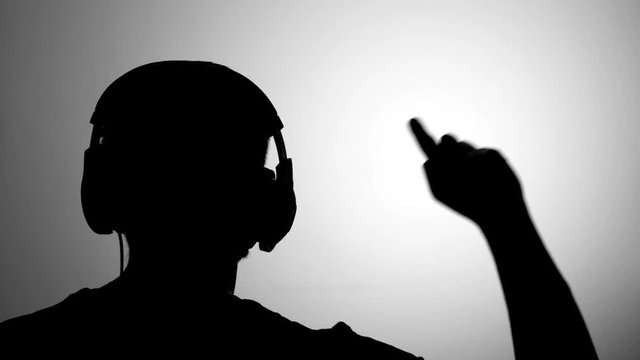 Mens black silhouette against grey wall listen to music wearing headphones, pointing his finger up