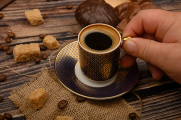 The girl's hand holds a Cup of coffee over a wooden table with brown sugar, coffee beans and chocolate.
