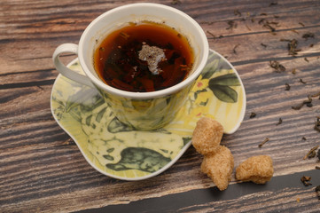 A Cup of black tea, tea leaves, brown sugar on a wooden background. Close up.