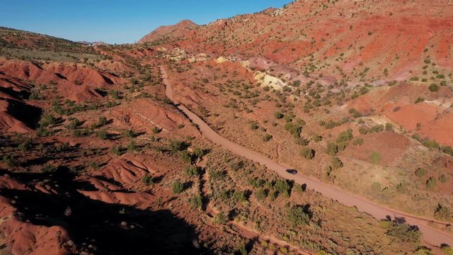 Black SUV Riding On Ground Road Crossing A Desert With Red Sand Dunes And Rocks