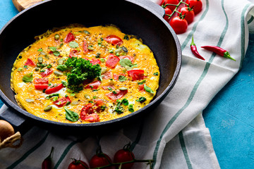 cast iron frying pan with fried scrambled eggs with herbs, cherry tomatoes, pumpkin seeds and chili pepper on a kitchen towel with copy of space