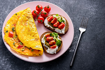 close up healthy Breakfast of egg omelet, wholegrain toast with cream cheese, pesto and cherry tomatoes on a pink plate, on a black stone background with a copy space.