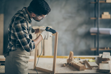 Profile side photo of serious concentrated worker man use electric hot glue gun to repair wooden construction frame work in home house garage - obrazy, fototapety, plakaty
