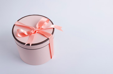 Pink cardboard box and peach colored ribbon and bow on the grey background.Gift box with bow