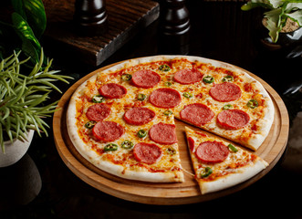 whole pepperoni pizza and a slice on wood pizza board
