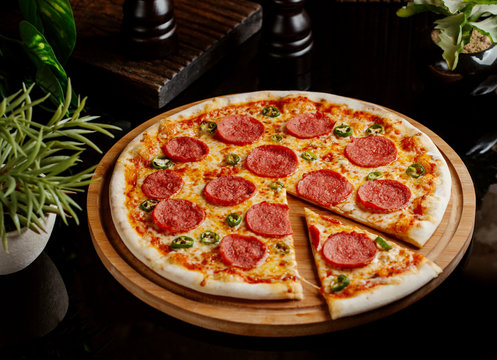 whole pepperoni pizza and a slice on wood pizza board