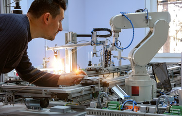 industry 4.0 concept: Man (engineer) is holding product and teaching robot arm the positions with...