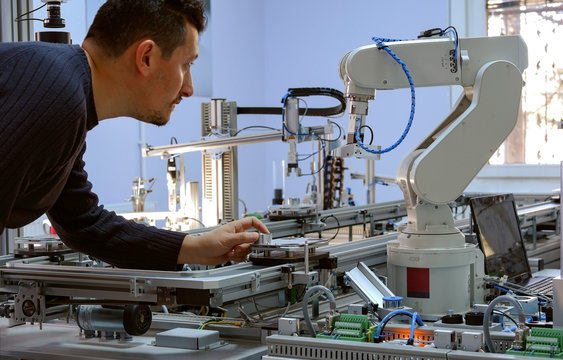 industry 4.0 concept: A mechatronics engineer is holding product and teaching robot arm the positions with teach pendant on smart factory production line background. Selective Focus.