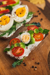 bruschettas on dark bread with curd cheese, eggs, vegetables, spices and herbs on a wooden board